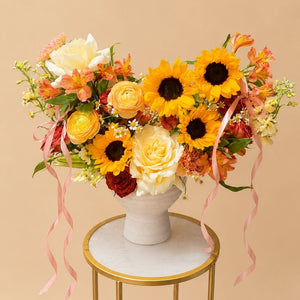 Golden Élan flower arrangement with golden sunflowers, cream roses, peach ranunculus, Alstroemeria, chamomile, and blush ribbon — Floral Savour Orlando florist.