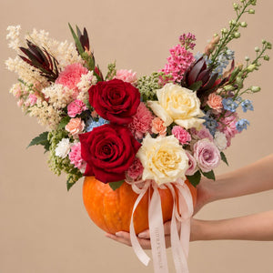 Designer’s Choice flower pumpkin arrangement with seasonal fall flowers in red, orange, peach, and green.